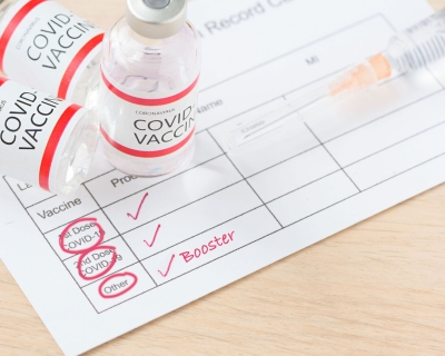 covid-19 vaccine vials and syringe laying on top of vaccine card