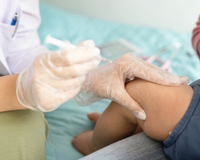 A doctor holding a syringe squeezes the thigh of a baby held by its parent